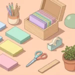 Pastel desk scene with five colored stacks of blank cards, a card box, scissors and a plant on a peach background.